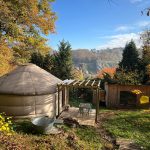 Yourte contemporaine avec terrasse, pergola, annexe et bain nordique surplombant la vallée de la Meuse en automne.